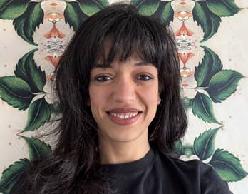 Yasmine, smiling, with some cool leafy wallpaper probably in the background